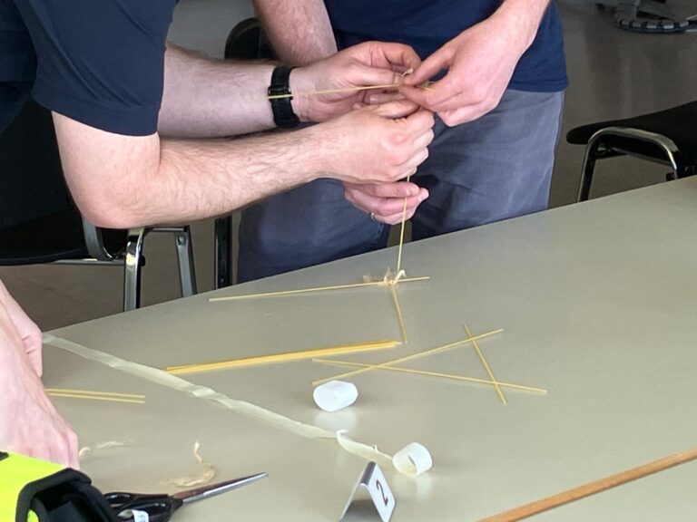 Teilnehmende bauen bei einer Teamübung einen Turm aus Spaghetti